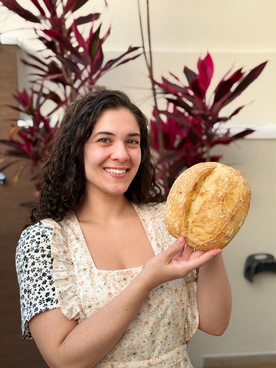 Gi, criadora do curso, segurando um pão de fermentação natural feito por ela